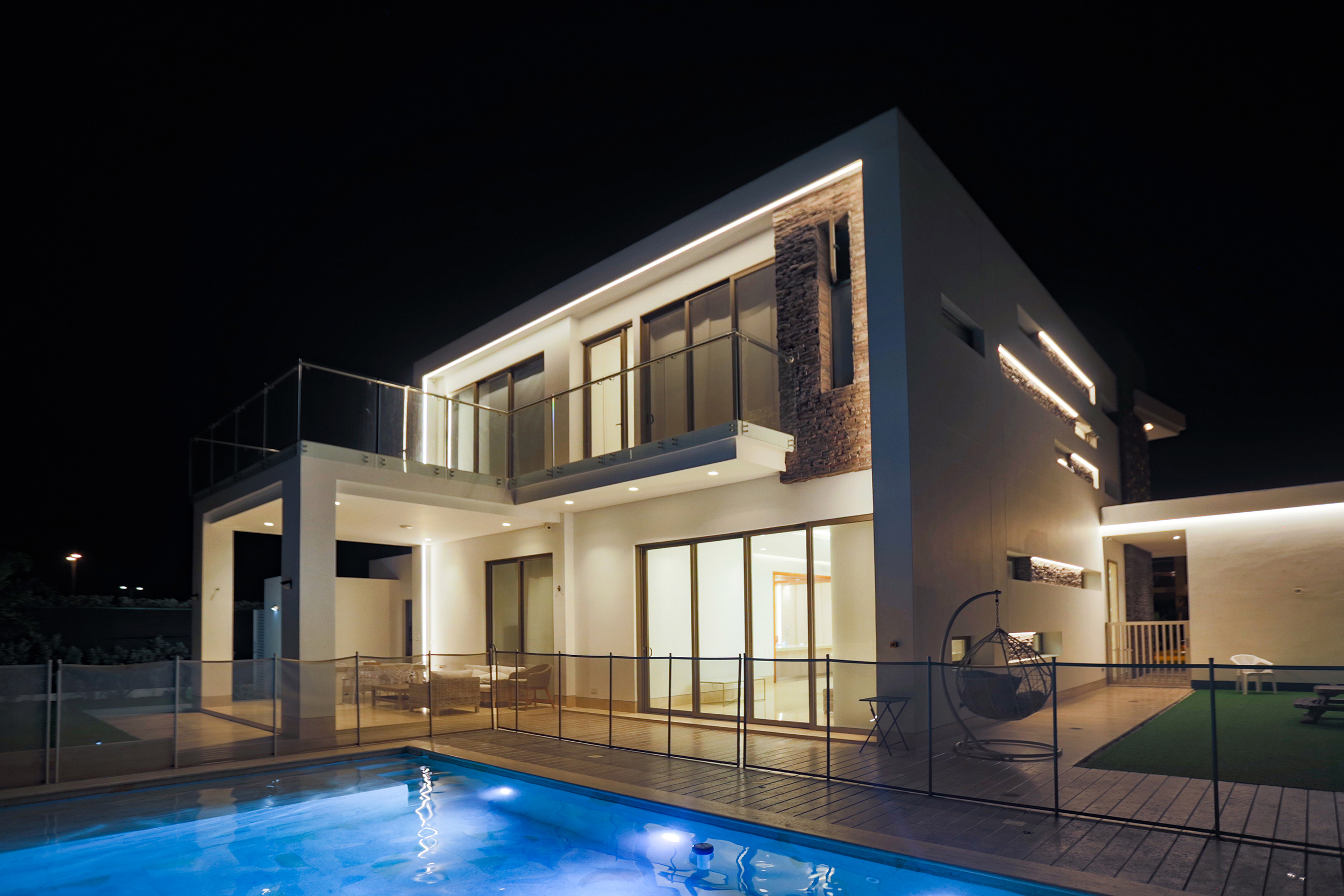 Fachada posterior iluminada de Casa Sarria 31 03 y piscina — ambiente nocturno.