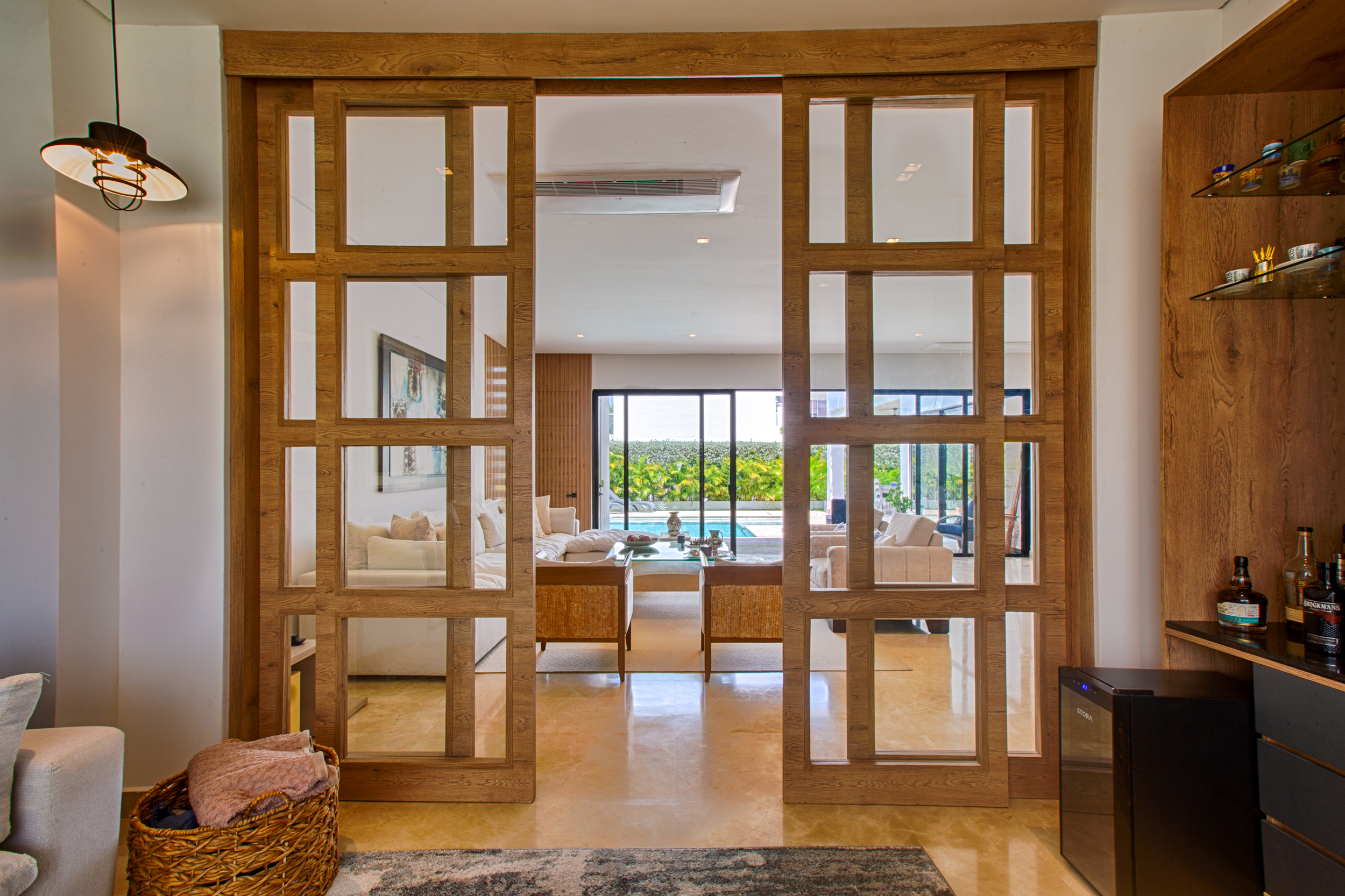 Puertas corredizas en madera y vidrio que conectan la zona social de Casa Sarria 15|04 con sala, piscina y diseño interior cálido de Topp Create.